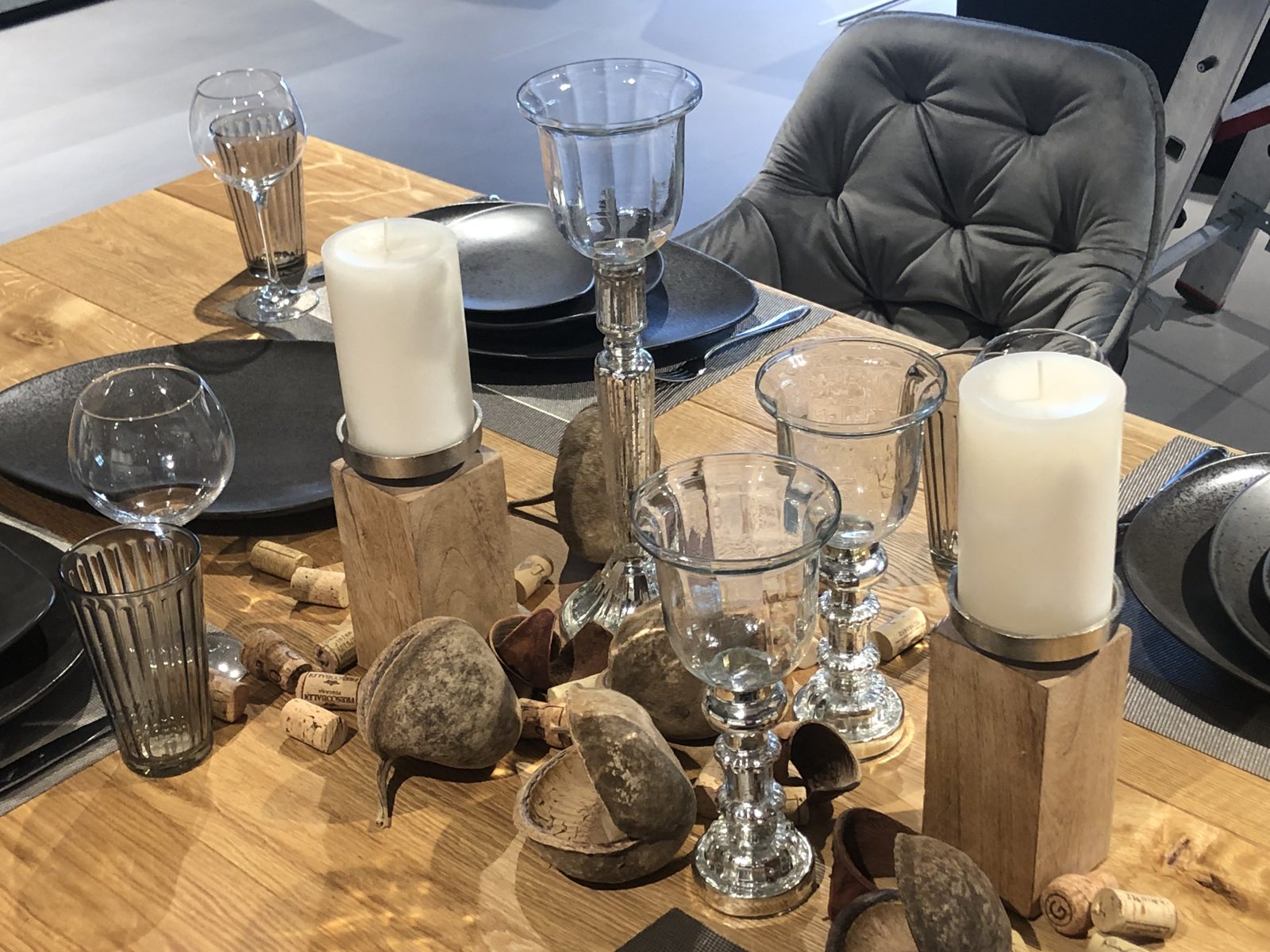 Gedeckter Holztisch mit Kerzen auf Holzblöcken, Glaswindlichtern und Korken
