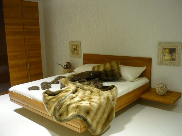Schwebendes Holzbett mit Felldecke und Kissen