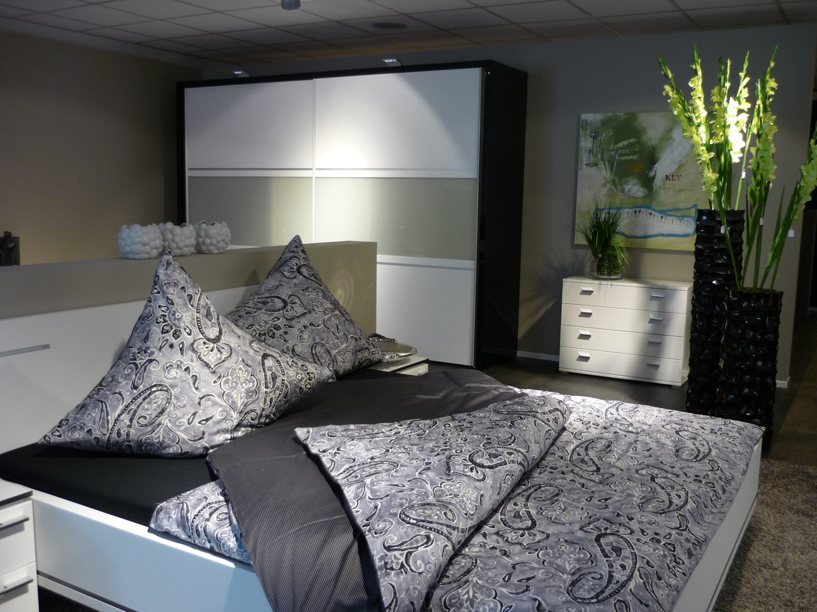 Schlafzimmer mit Paisley-Bettwäsche, Gladiolen in schwarzen Vasen und Bild